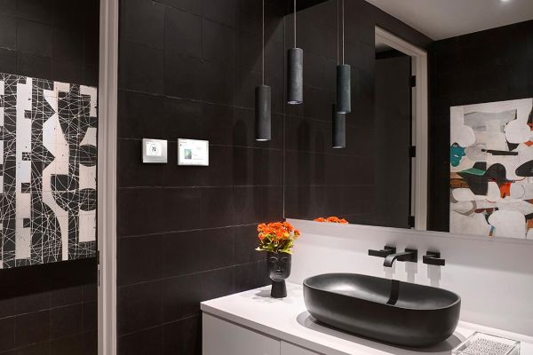 A sleek bathroom with dark tiles, modern pendant lights, and a stylish black basin on a floating vanity, accented with bright flowers.