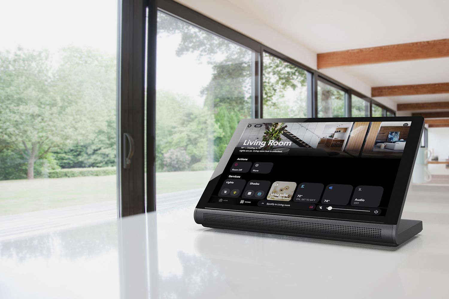 A smart home control display on a white counter with large windows overlooking a green garden in the background.