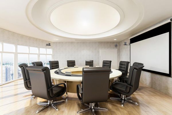 A round boardroom with a large circular table, leather chairs, and floor-to-ceiling windows offering city views.