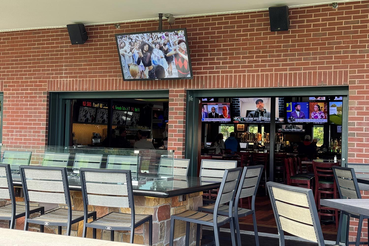 An outdoor seating area of a restaurant with televisions displaying various channels to patrons inside.