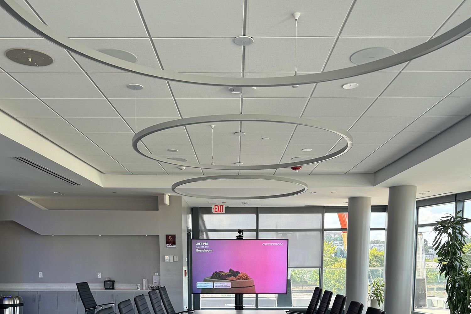 Circular light fixtures on a modern ceiling above a conference room with a screen at the far end.