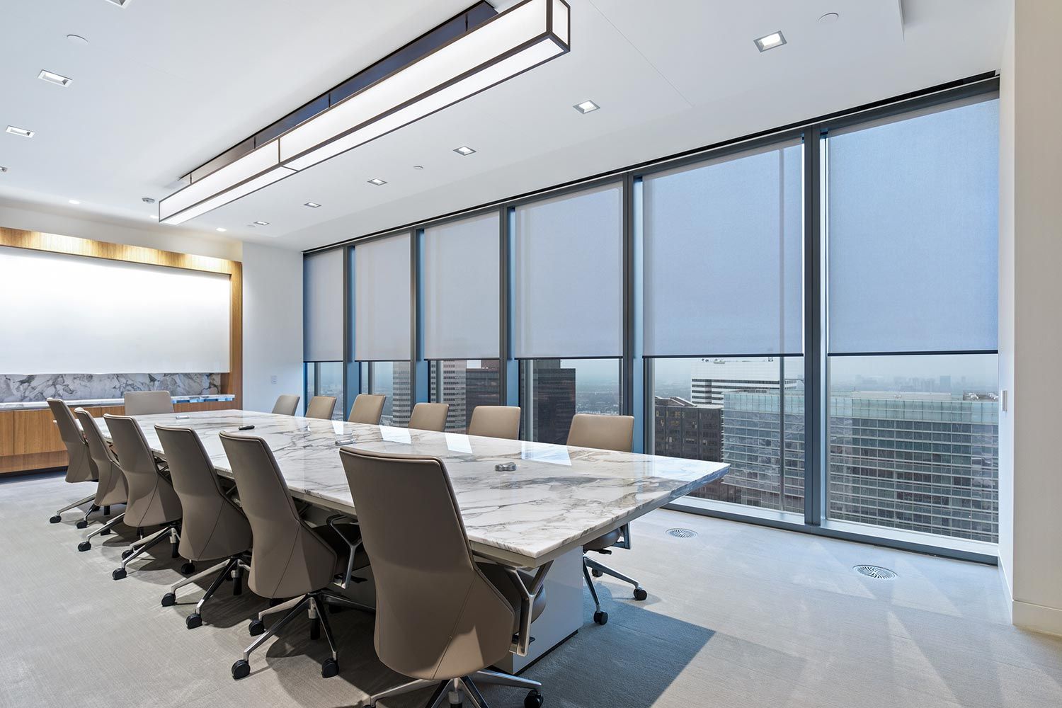 Modern conference room with large motorized window shades partially drawn, overlooking a city skyline.