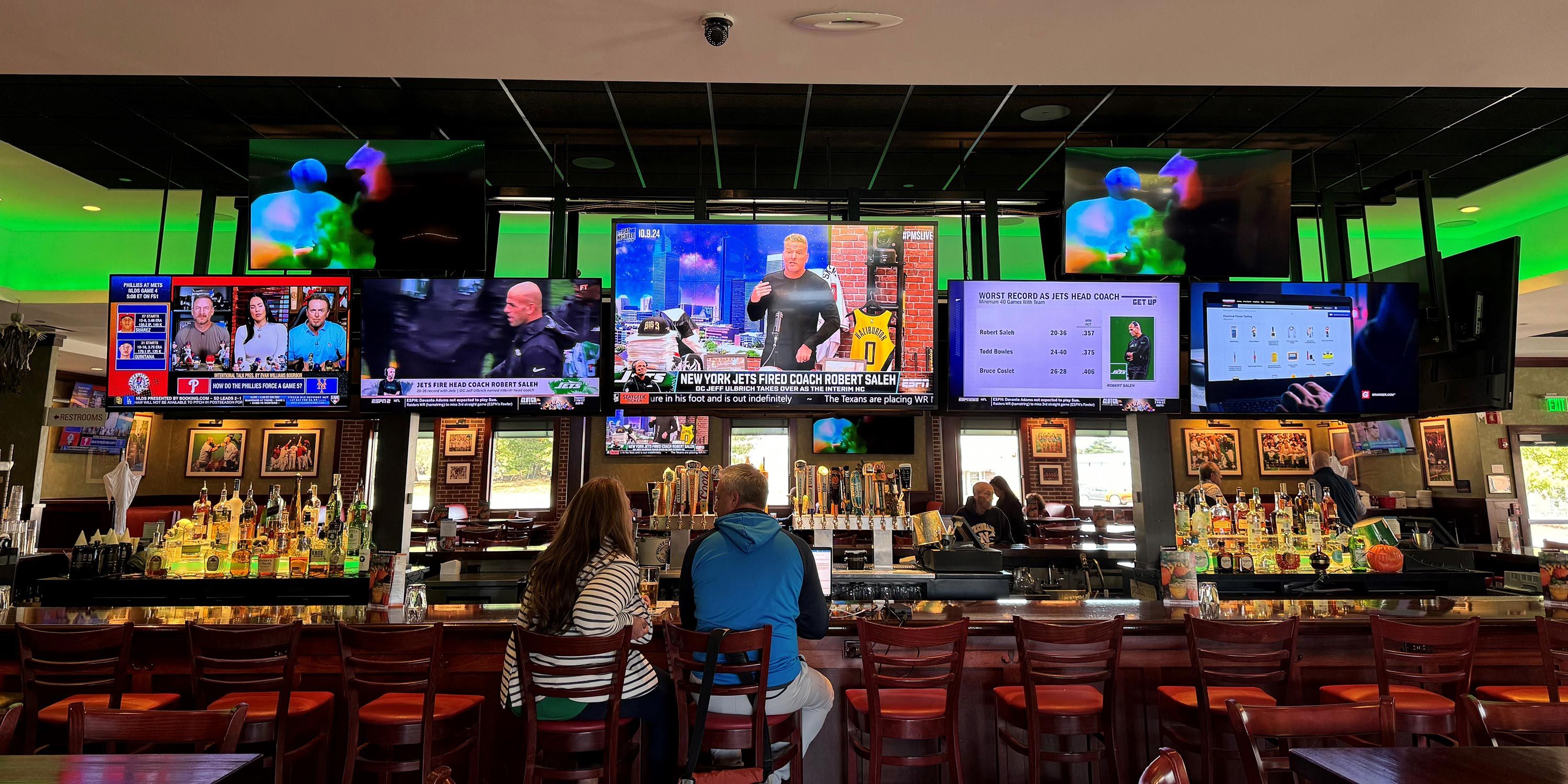 A lively sports bar with multiple screens showing different sports events and a long bar counter.