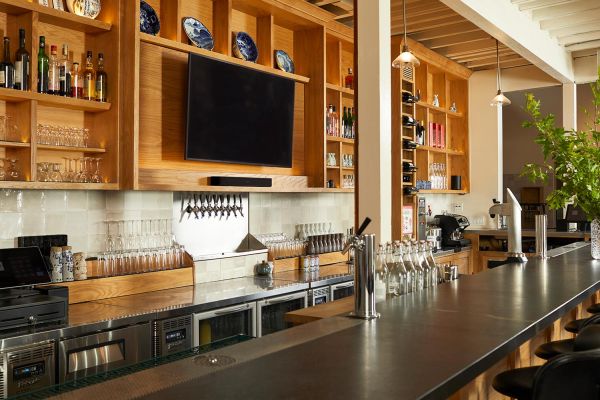 A stylish bar area with warm wooden shelving, a mounted TV, and a polished countertop, showcasing a cozy and modern aesthetic.