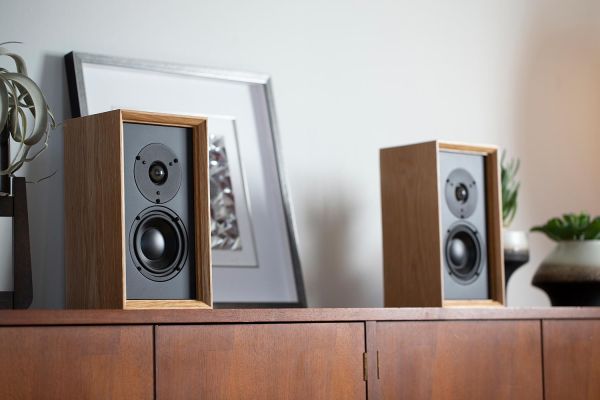 Close-up of two minimalist bookshelf speakers with wood accents, set on a mid-century modern cabinet.