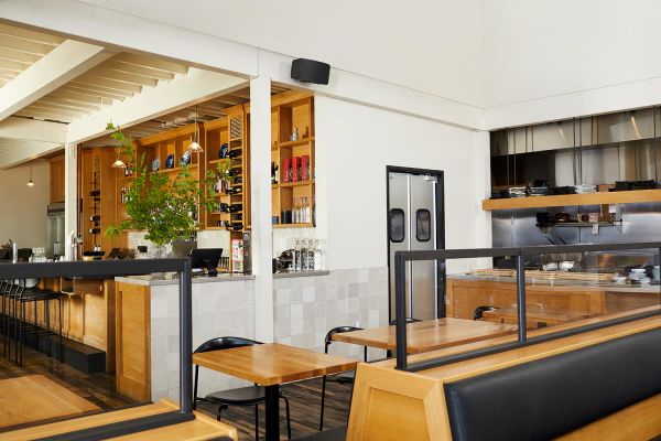 A modern dining area with booth seating, a view into the kitchen, and natural wood finishes, creating a casual yet elegant atmosphere.