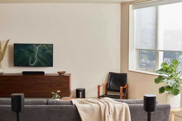 A living room setup with a wall-mounted TV, dark wooden console, and a cozy gray sofa with sound equipment arranged around the space.